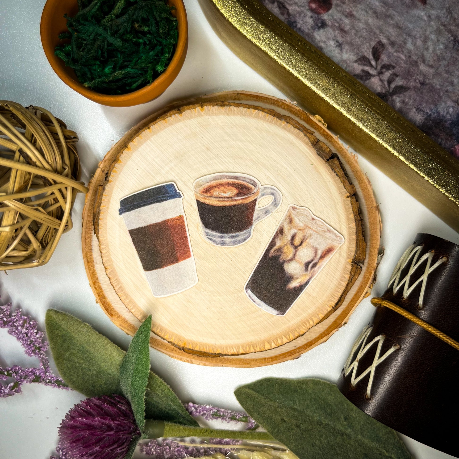Wooden coaster with 3 Mini Coffee Stickers featuring hand drawn Espresso, Iced Coffee, and a To-Go Cup sitting on a decorative surface with plants and a gold box.
